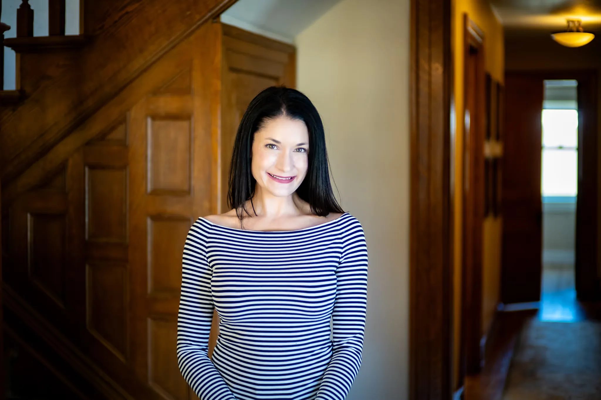 A Nelson Law Firm staff member in a striped top standing with a hand on hip in a wood-trimmed hallway of the firm's Denver office