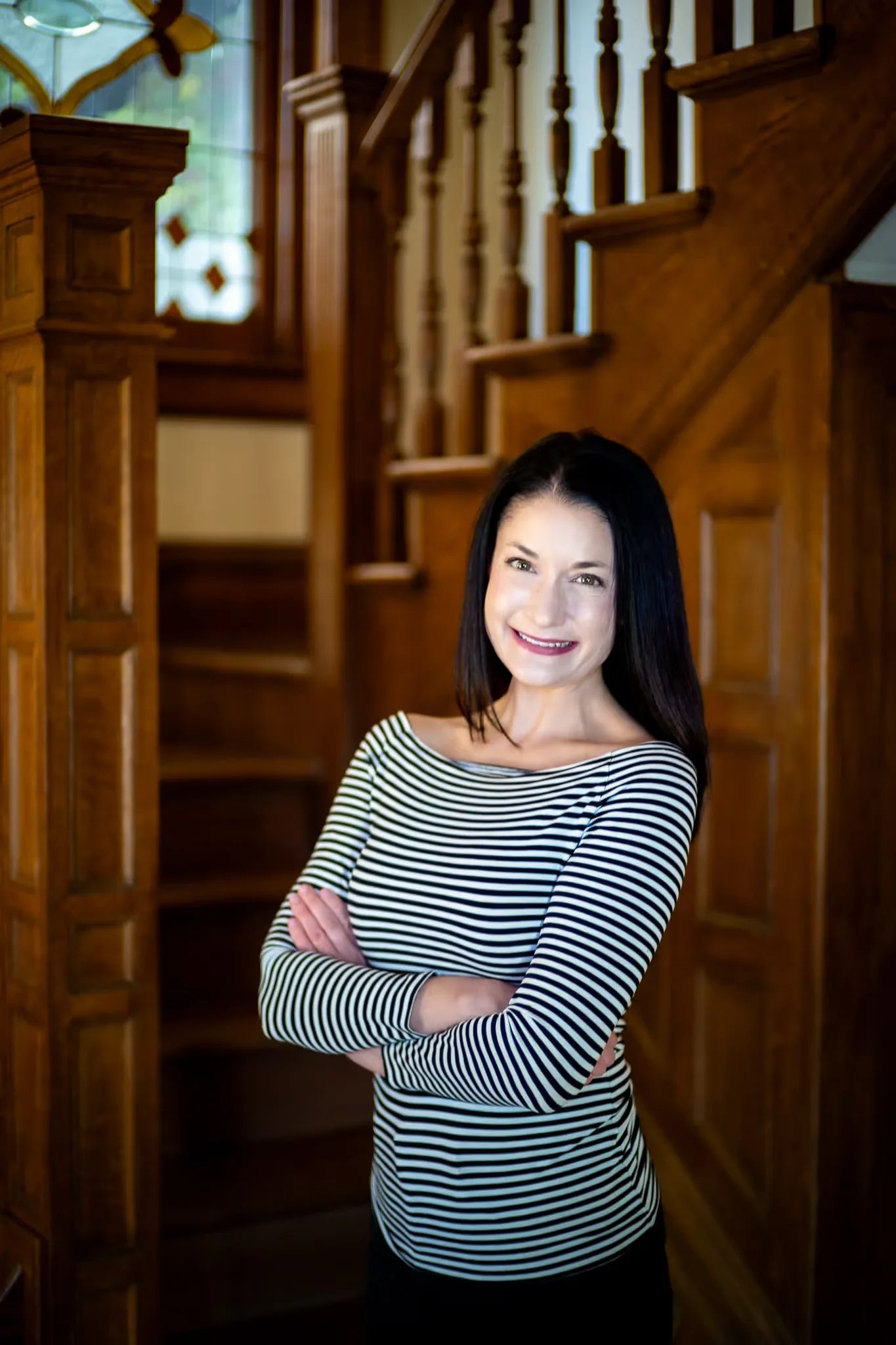 A Nelson Law Firm staff member in a striped top with arms crossed at the stained-glass staircase of the firm's Denver office
