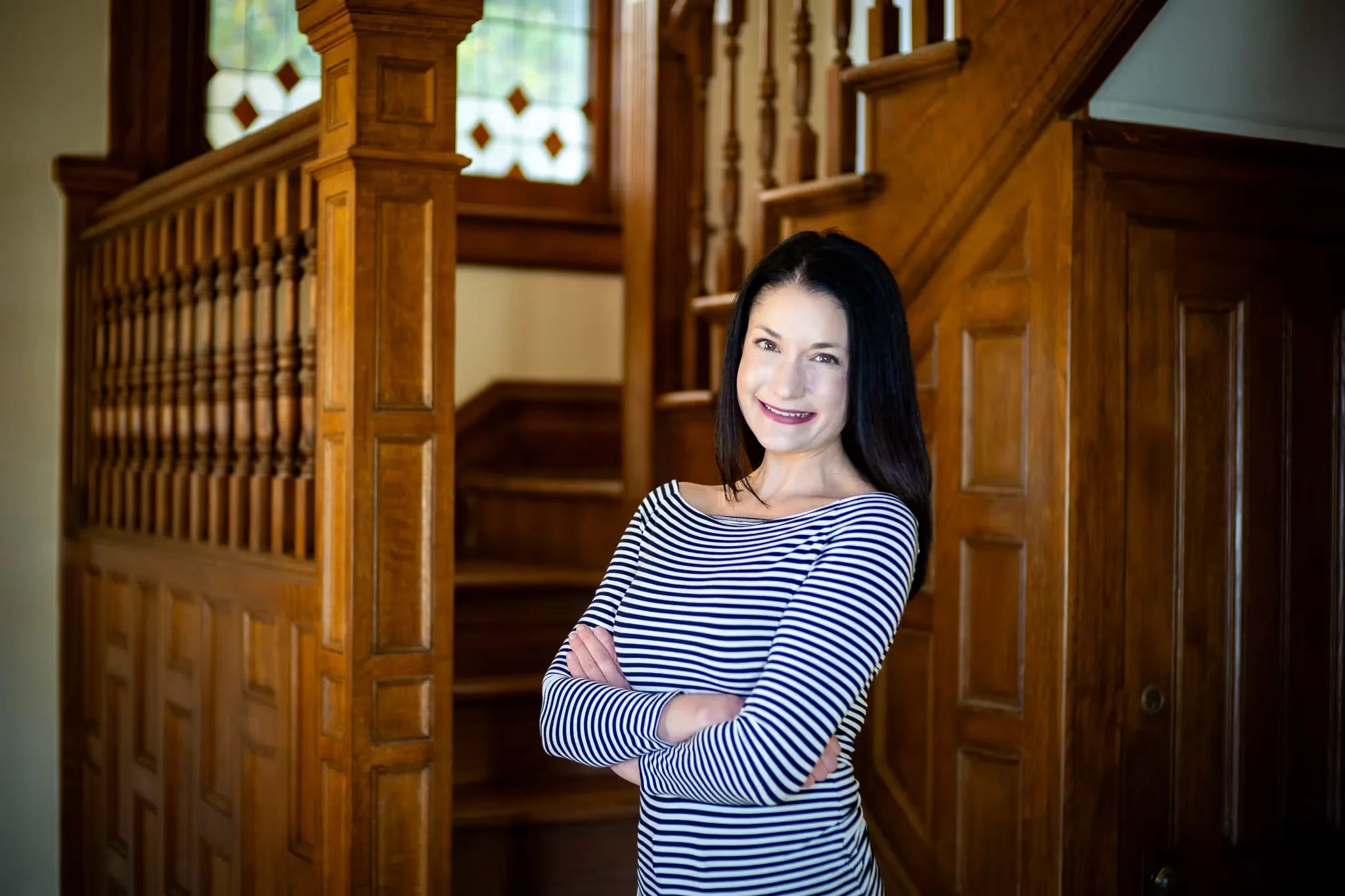 A Nelson Law Firm staff member in a striped top with arms crossed in front of the oak staircase in Denver