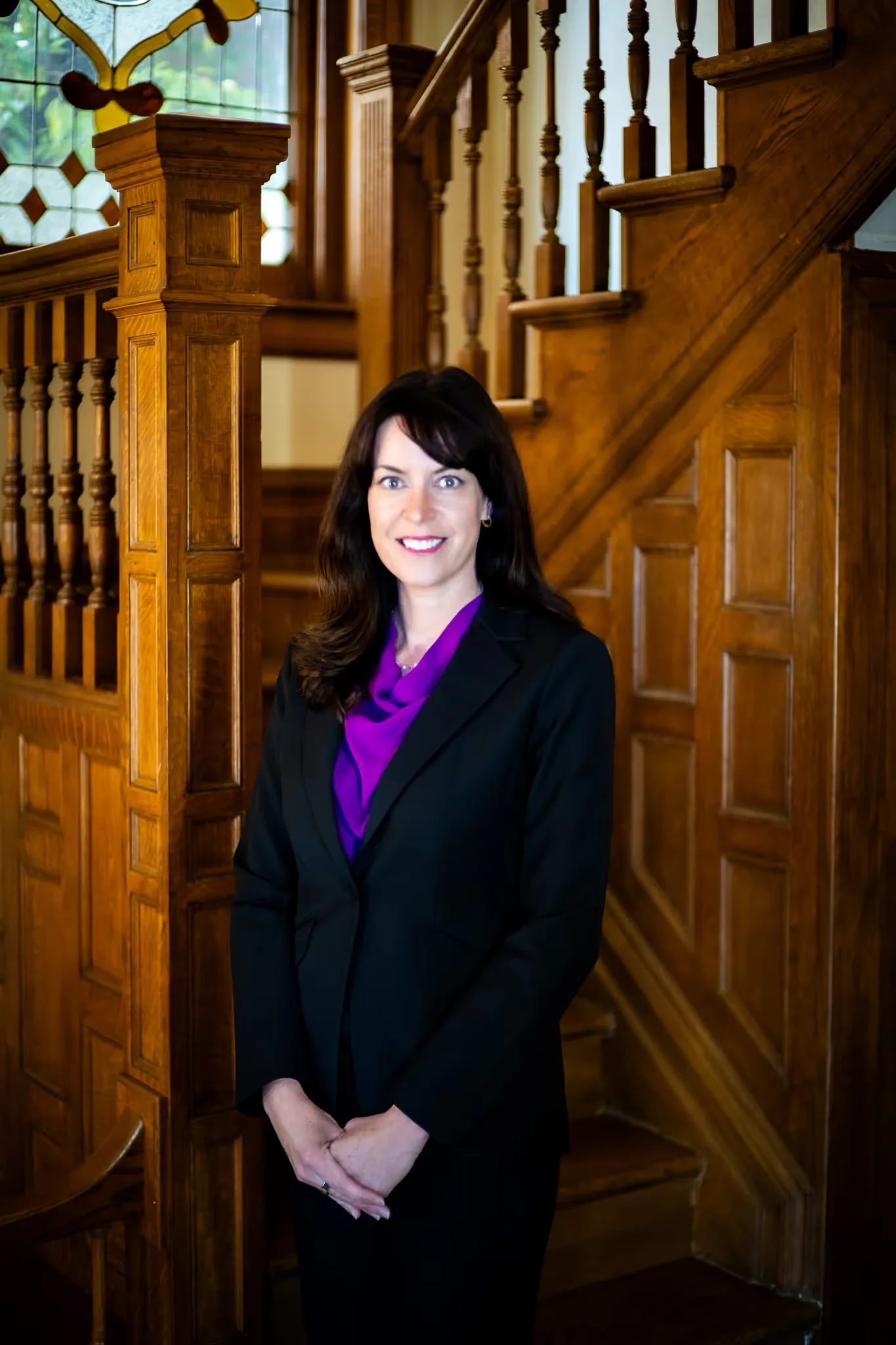 Colleen S. Nelson, co-founder of Nelson Law Firm, in a purple blouse and black blazer at the oak staircase of the firm's Denver office