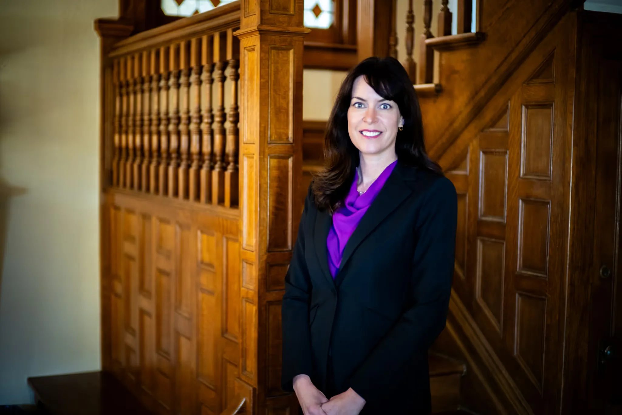Colleen S. Nelson, co-founder of Nelson Law Firm, smiling with hands clasped in front of the firm's oak staircase in Denver