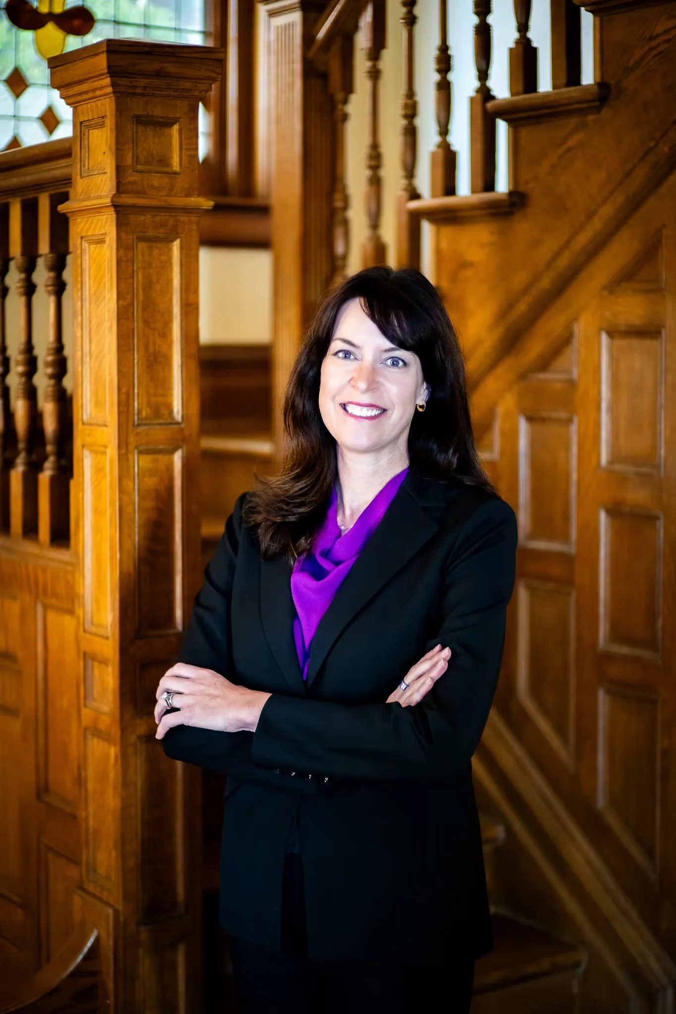 Colleen S. Nelson, co-founder of Nelson Law Firm, with arms crossed at the stained-glass staircase of the firm's Denver office