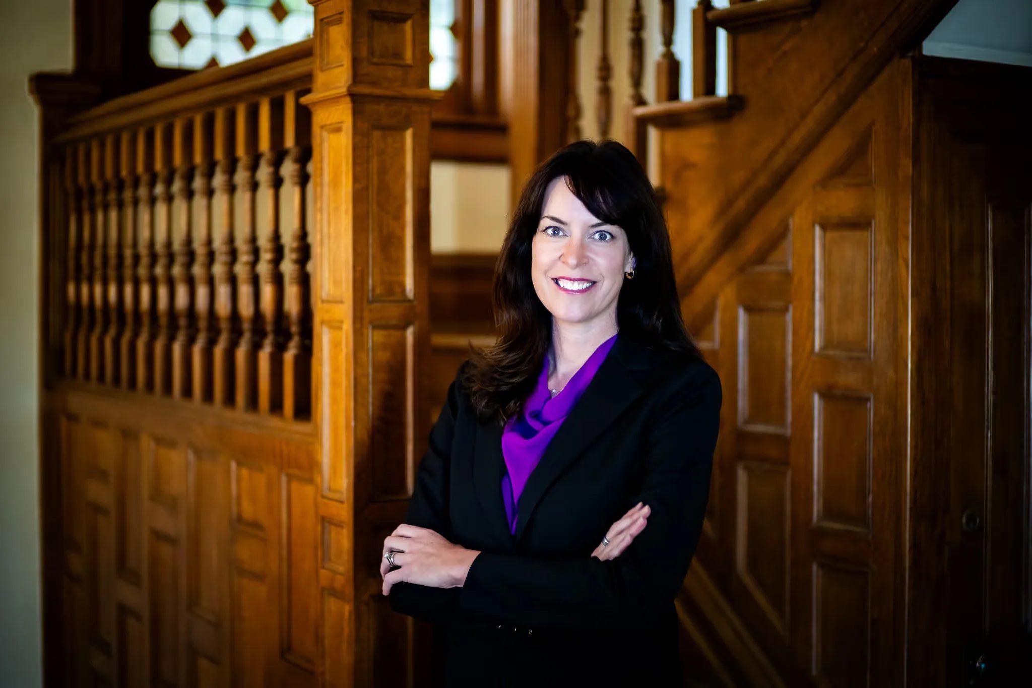 Colleen S. Nelson, co-founder of Nelson Law Firm, arms crossed and smiling beside the oak staircase of the firm's Denver office
