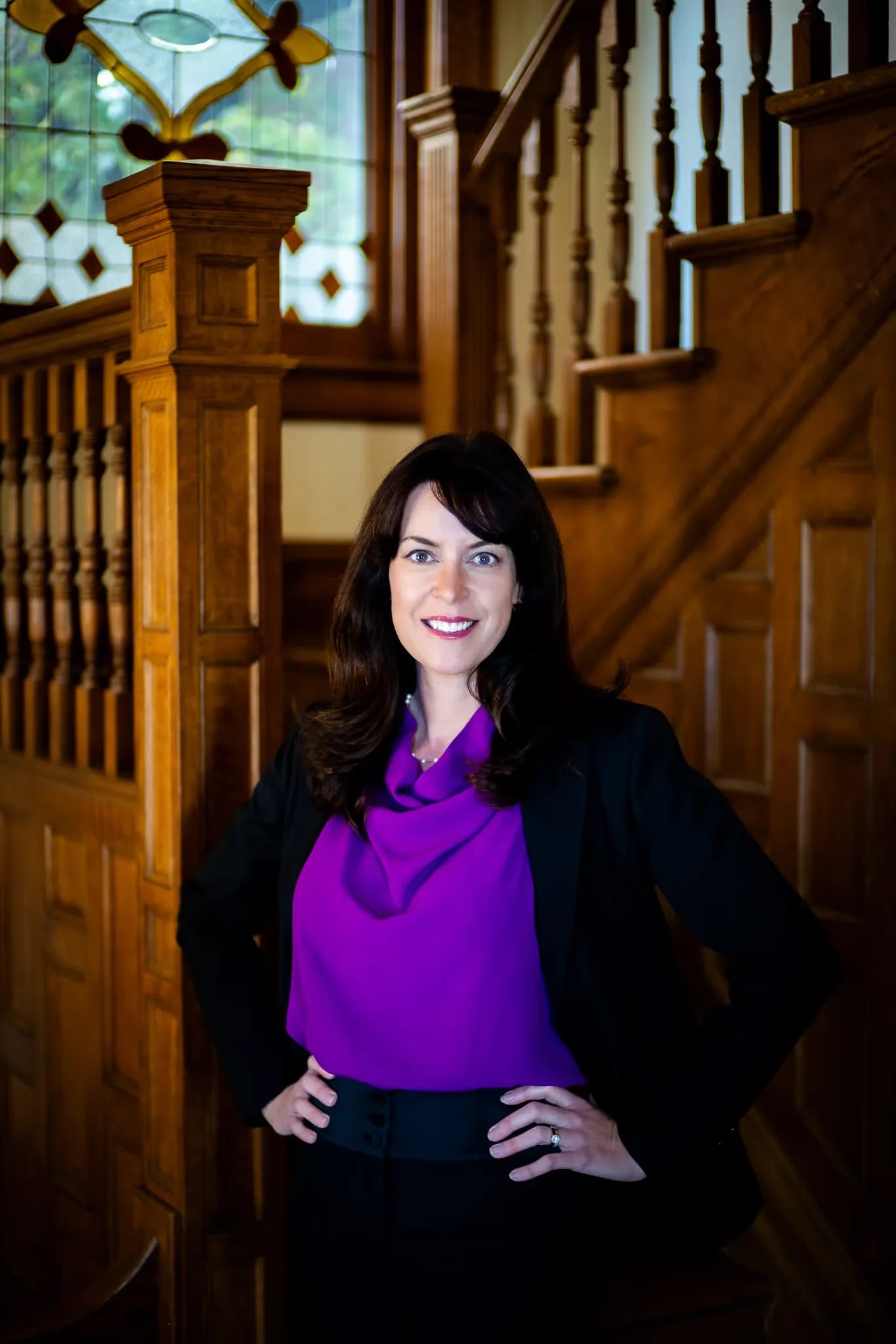 Colleen S. Nelson, co-founder of Nelson Law Firm, with a hand on hip at the stained-glass staircase of the firm's Denver office