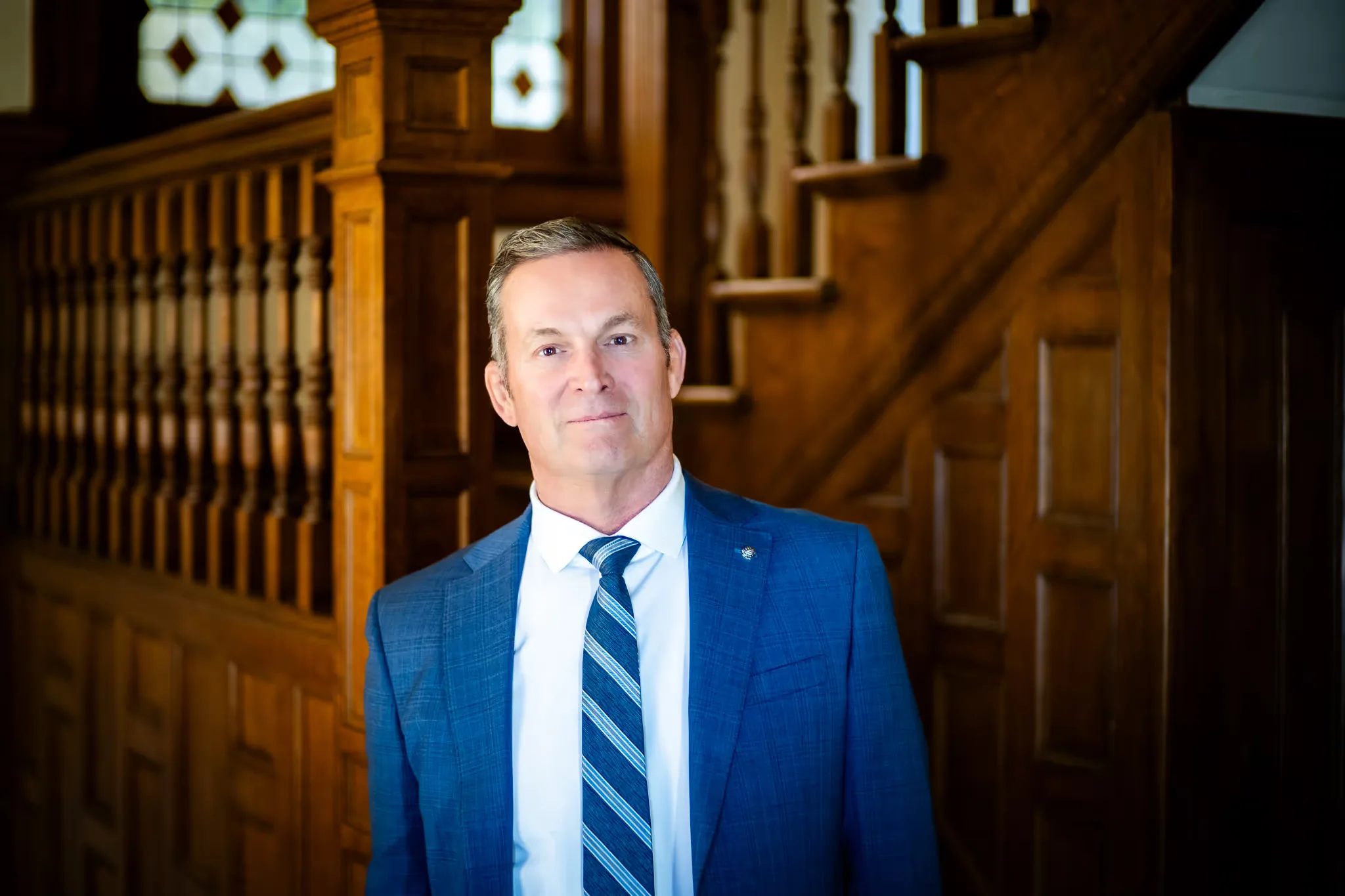 Mark W. Nelson, founder of Nelson Law Firm, in a blue suit and striped tie at the oak staircase of the firm's Denver office
