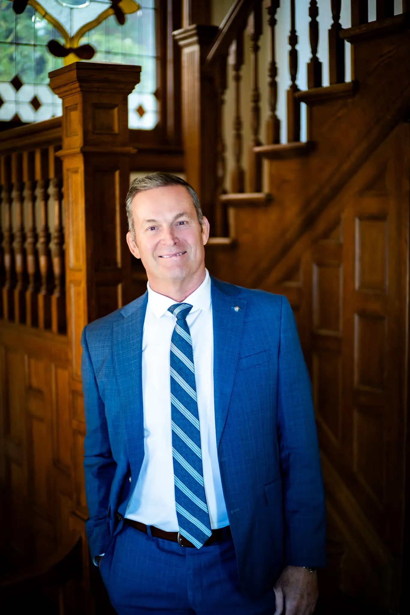 Mark W. Nelson, founder of Nelson Law Firm, in a blue suit at the stained-glass staircase of the firm's Denver office