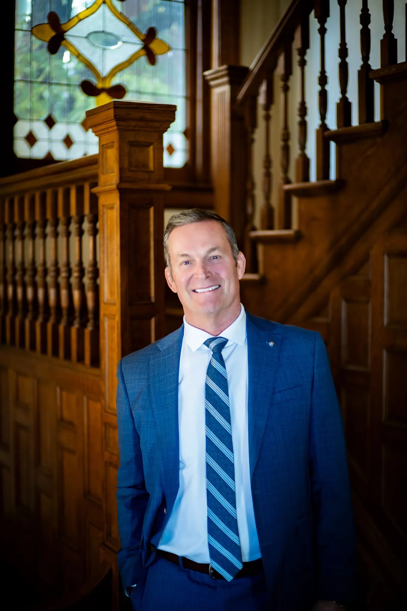 Mark W. Nelson, founder of Nelson Law Firm, smiling in a blue suit and striped tie at the firm's oak staircase in Denver