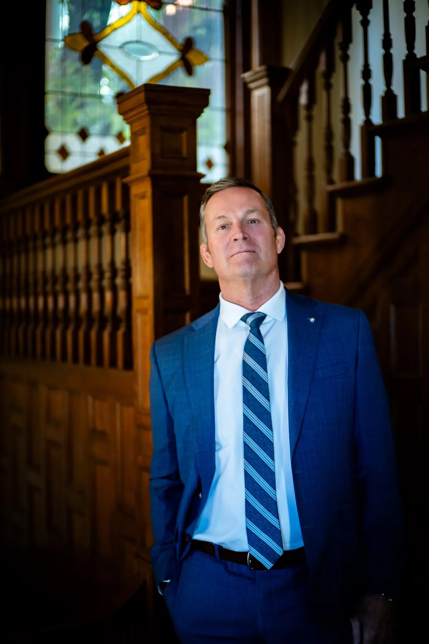 Mark W. Nelson, founder of Nelson Law Firm, in a blue suit beside the oak staircase of the firm's Denver office