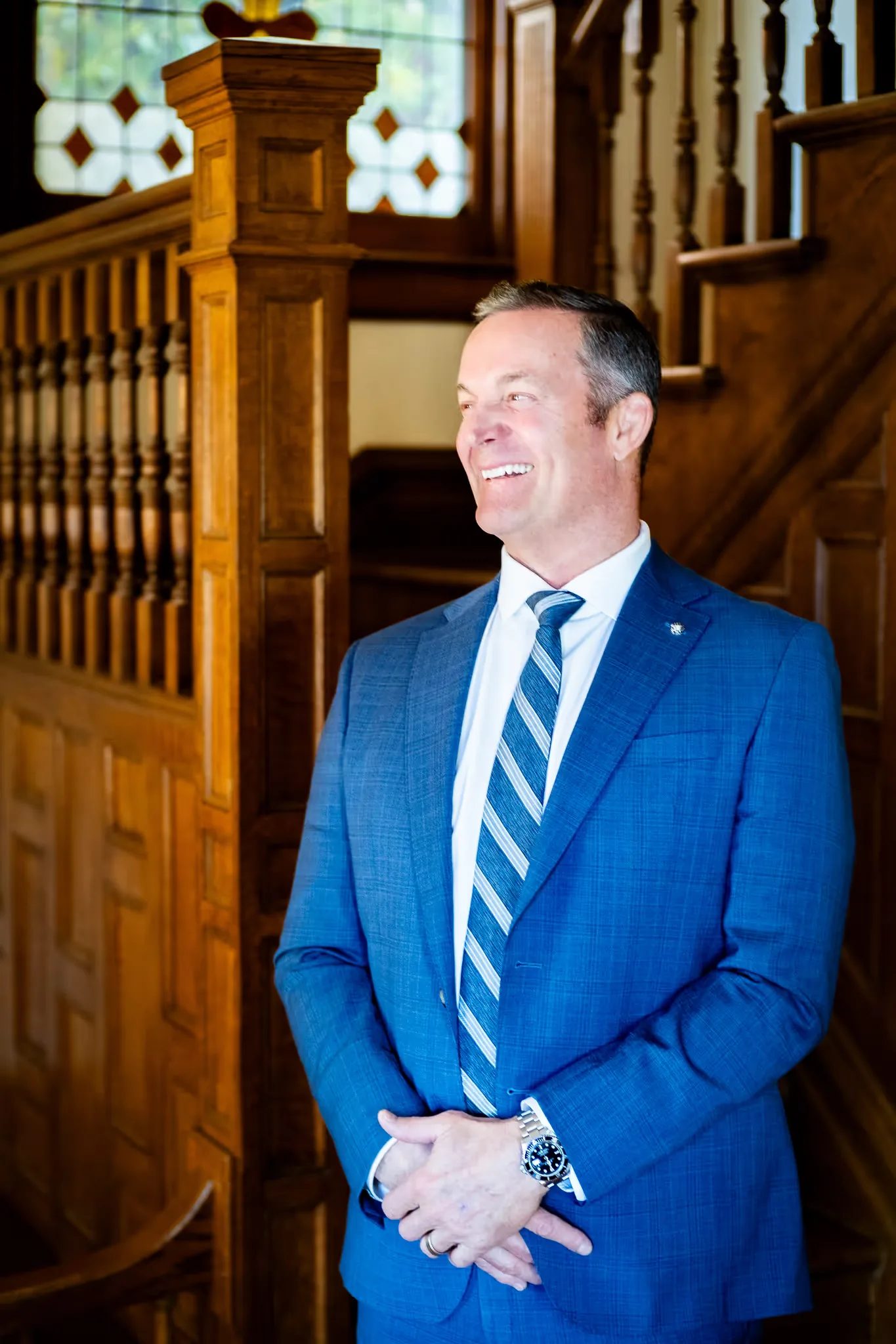 Mark W. Nelson, founder of Nelson Law Firm, smiling broadly with hands clasped at the firm's oak staircase in Denver