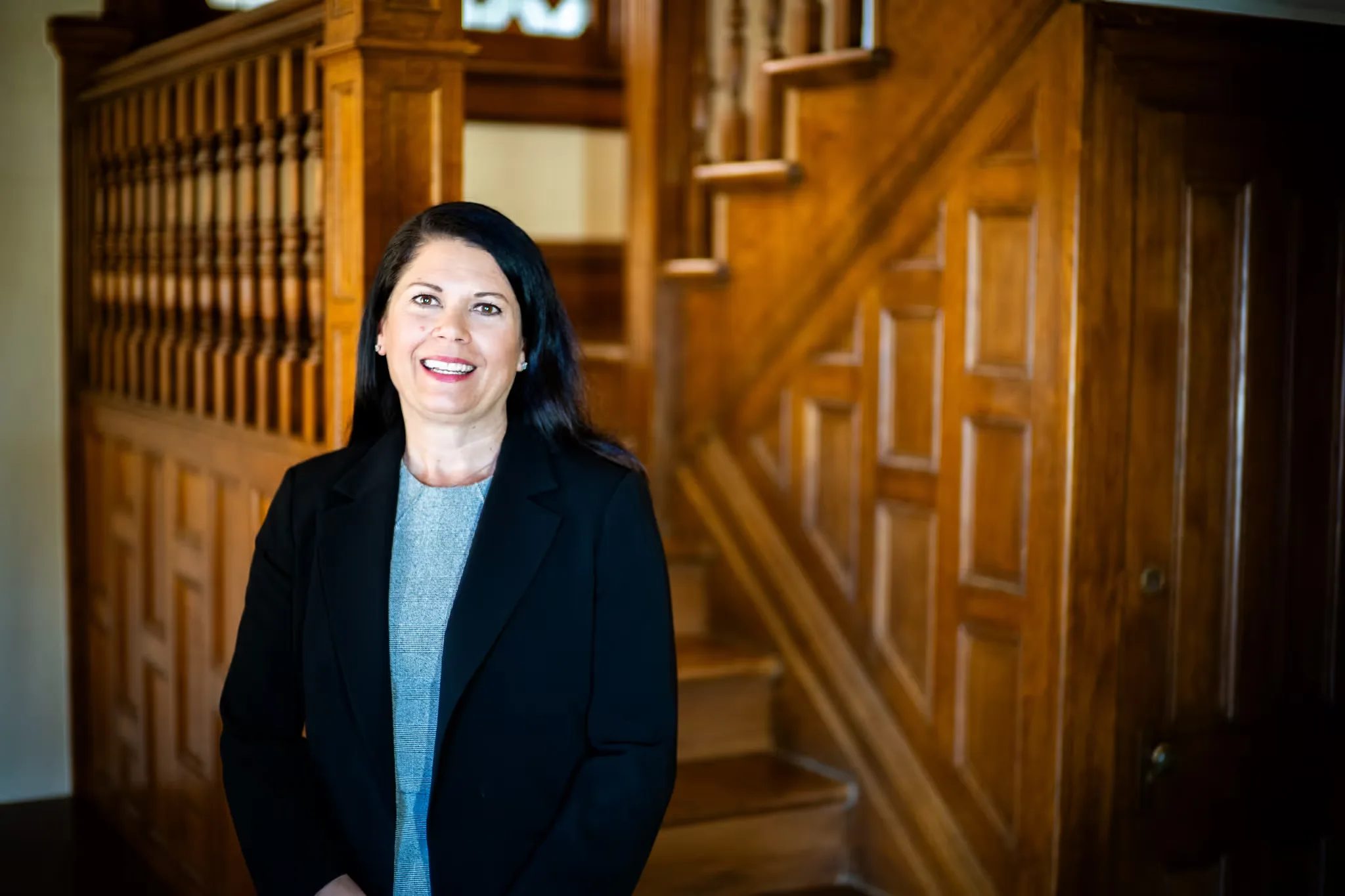 A Nelson Law Firm staff member in a black blazer with hands clasped in front of the oak staircase in the firm's Denver office