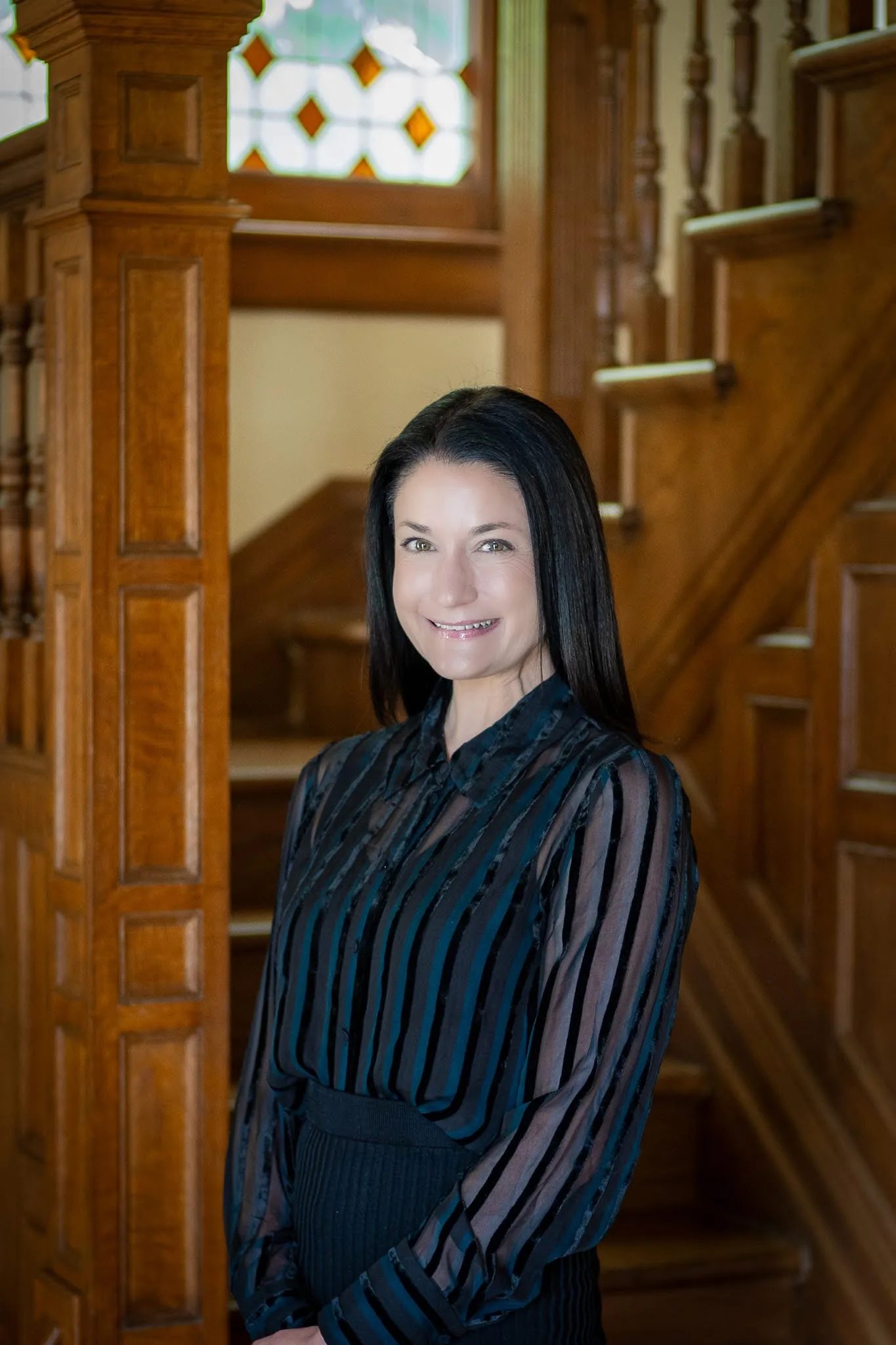 Ivy Sanders, senior paralegal at Nelson Law Firm, standing beside the oak staircase in the firm's Denver office