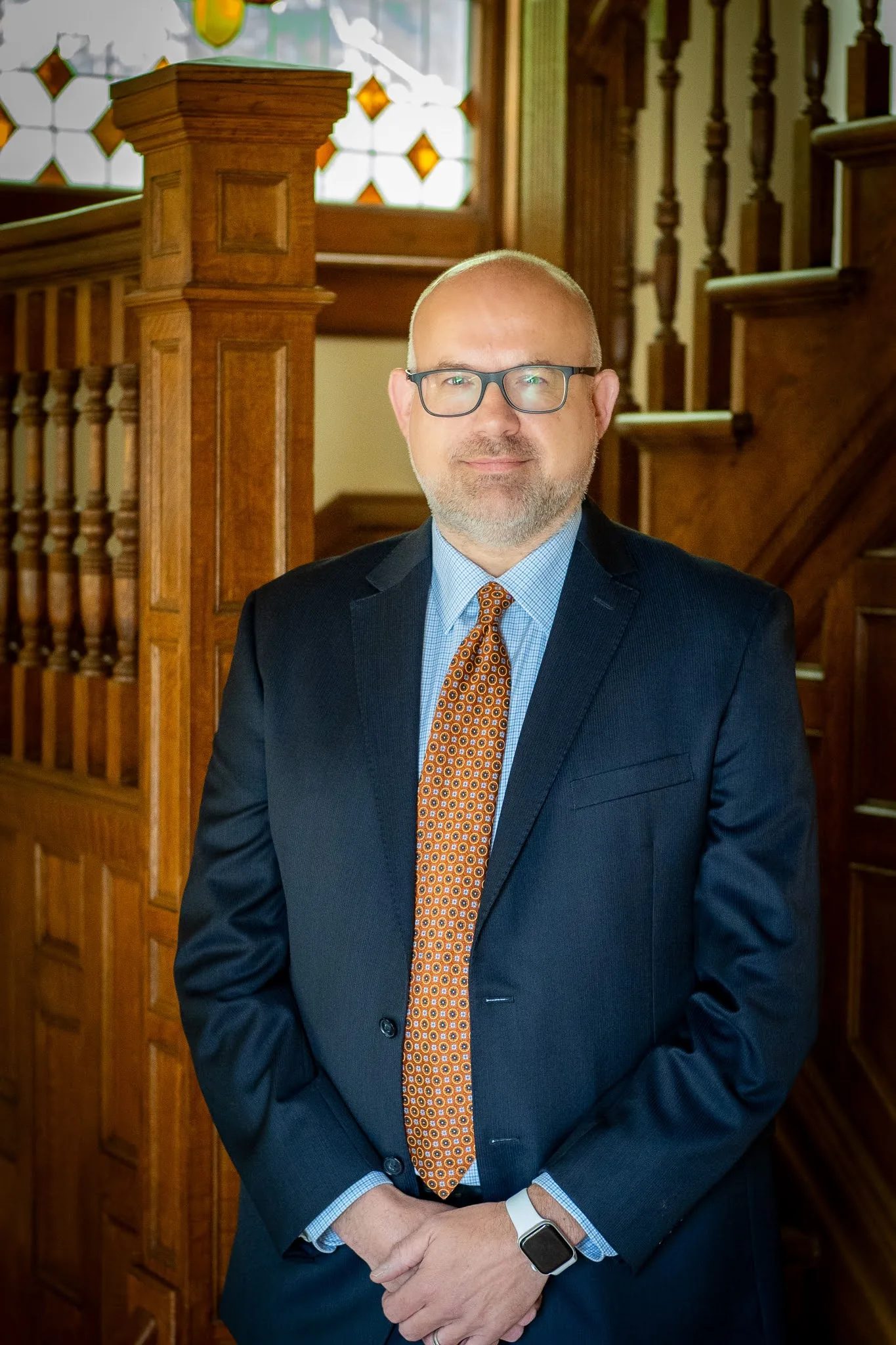 Kevin P. Ahearn, attorney at Nelson Law Firm, in a navy suit and orange tie at the oak staircase of the firm's Denver office
