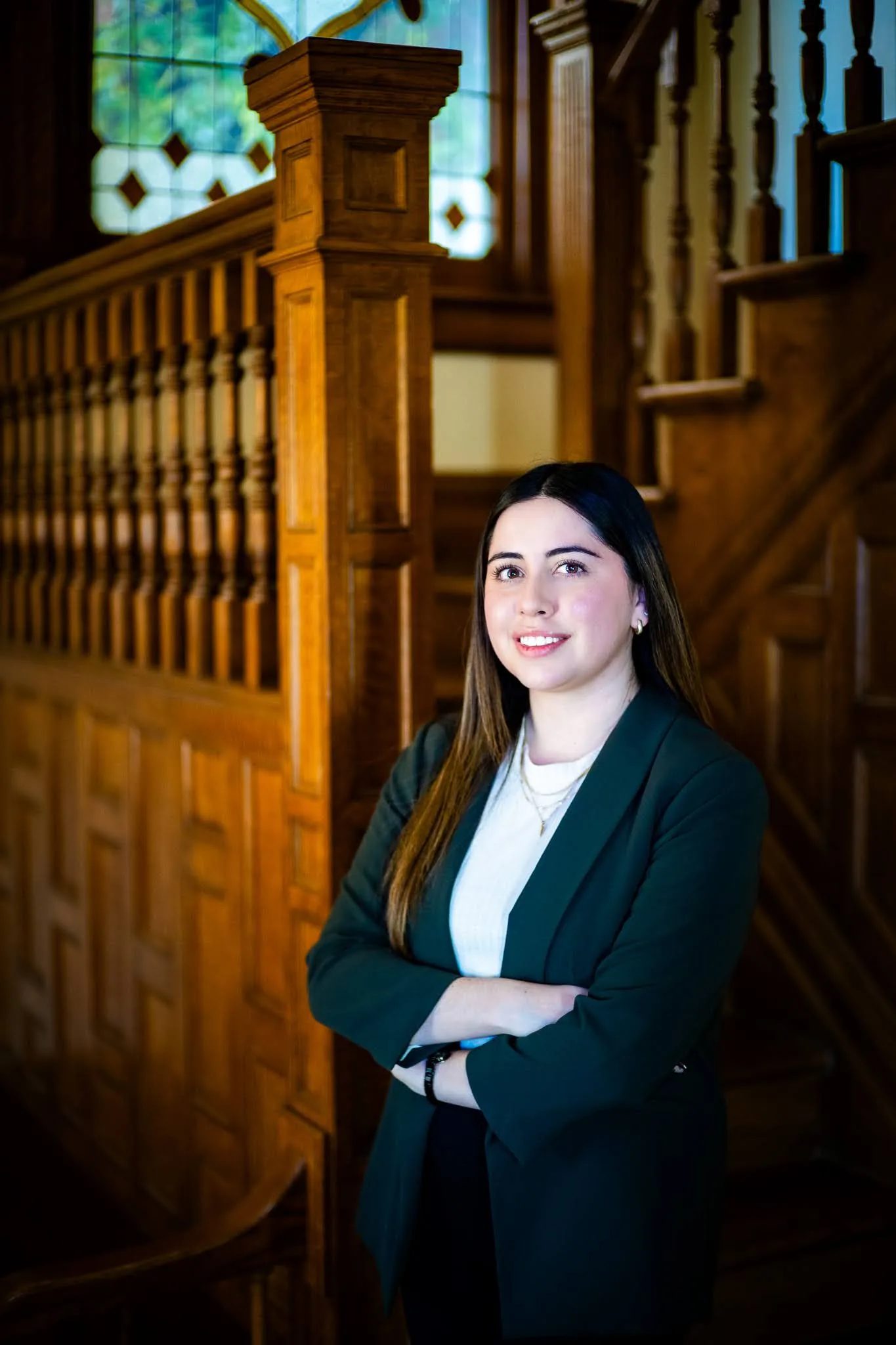 Mariana Gonzalez, paralegal, with arms crossed beside the oak staircase at Nelson Law Firm's Denver office
