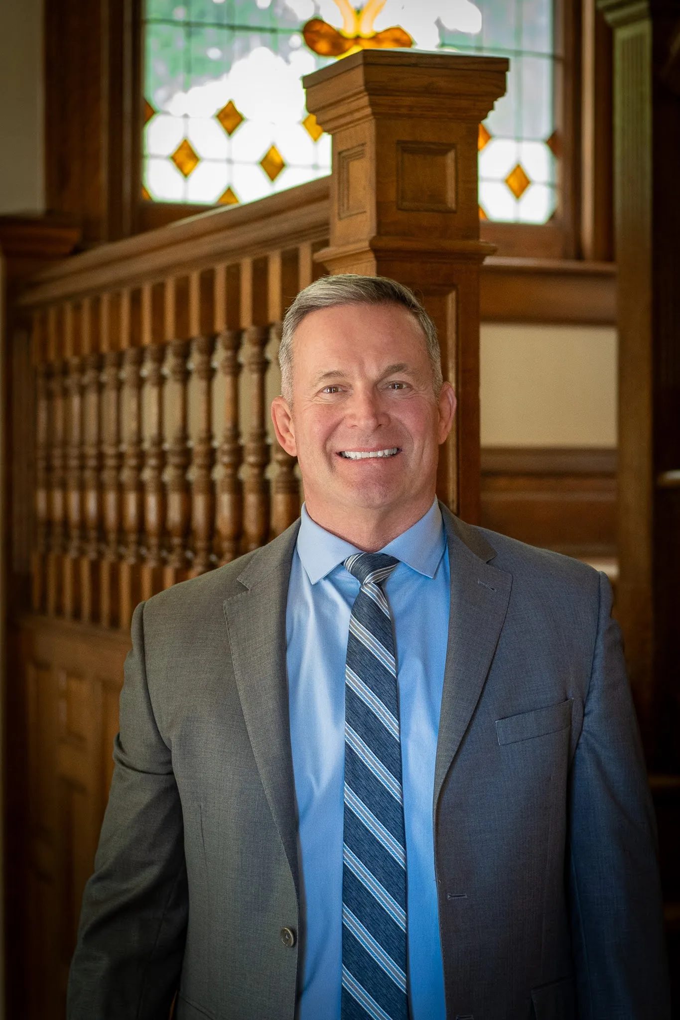 Mark W. Nelson, founder of Nelson Law Firm, smiling in a grey suit at the oak staircase of the firm's Denver office
