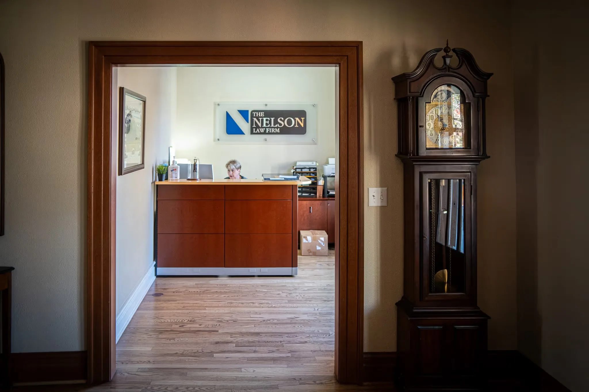 View through a wood-trimmed doorway to the Nelson Law Firm reception desk and wall sign, with a grandfather clock at right.