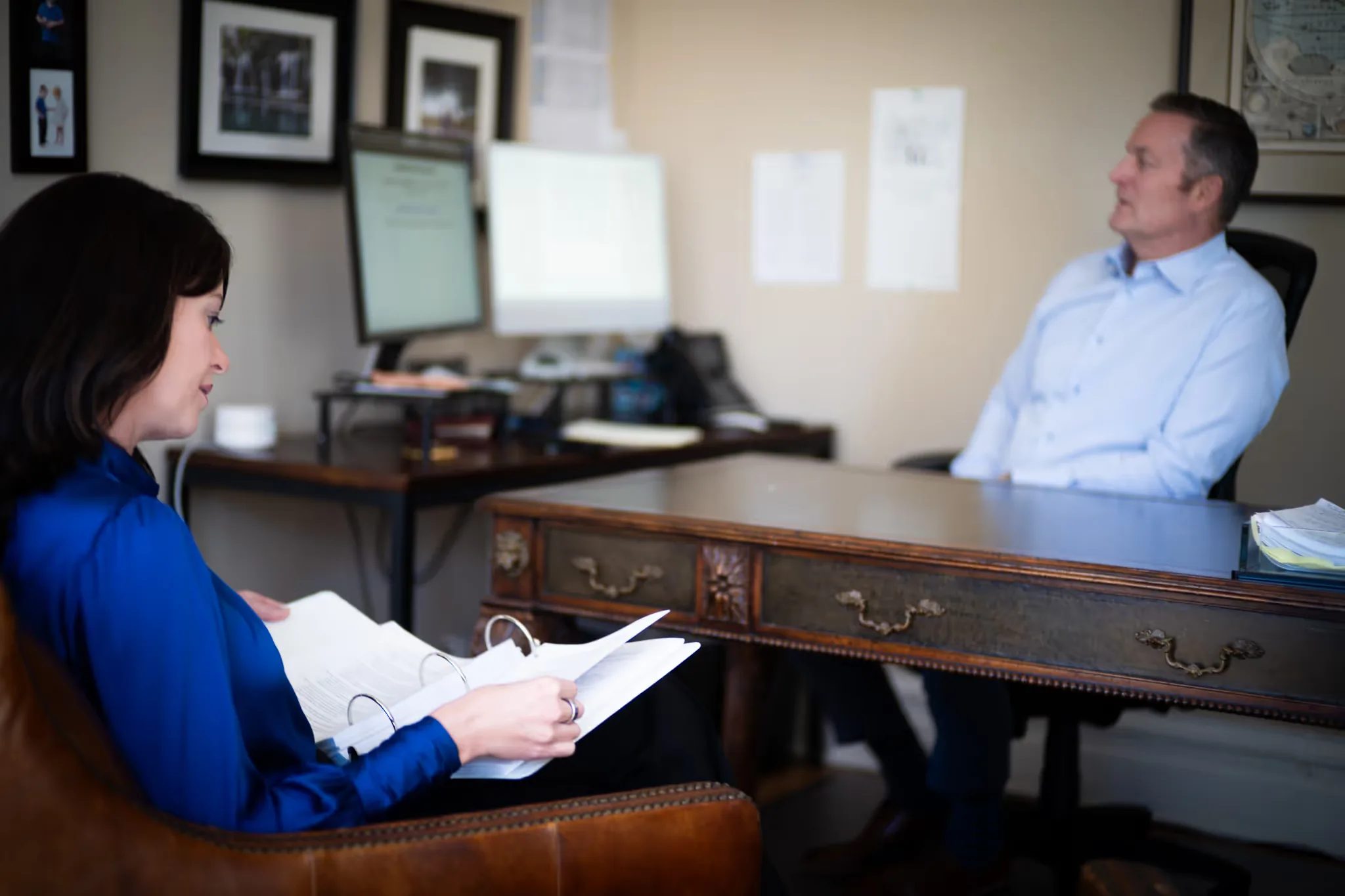 Mark W. Nelson at a desk talking with Colleen S. Nelson, who reads a document from an armchair in the Nelson Law Firm office