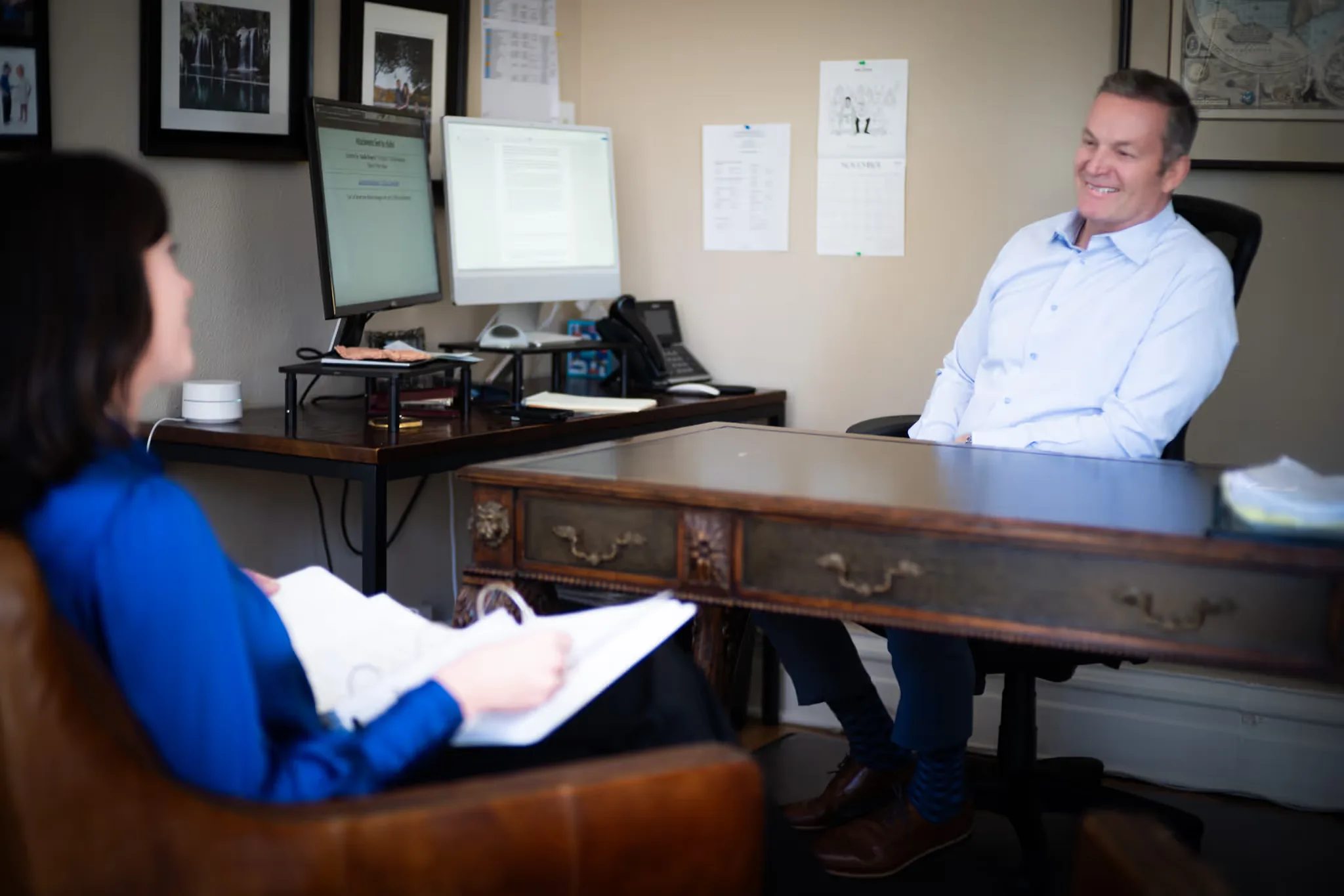 Mark W. Nelson smiling from a desk chair as Colleen S. Nelson reads a file in an armchair in the Nelson Law Firm office