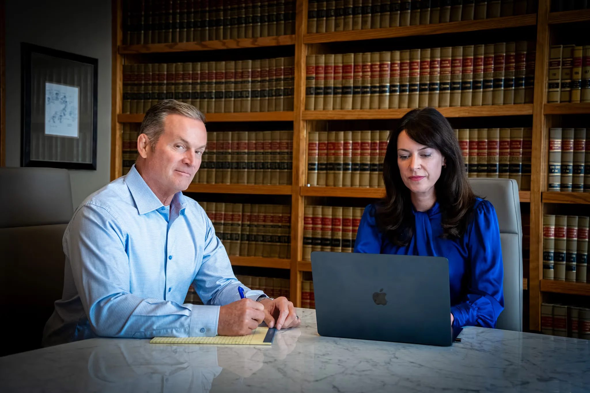 Mark W. Nelson writing on a legal pad while Colleen S. Nelson works on a laptop in the Nelson Law Firm library