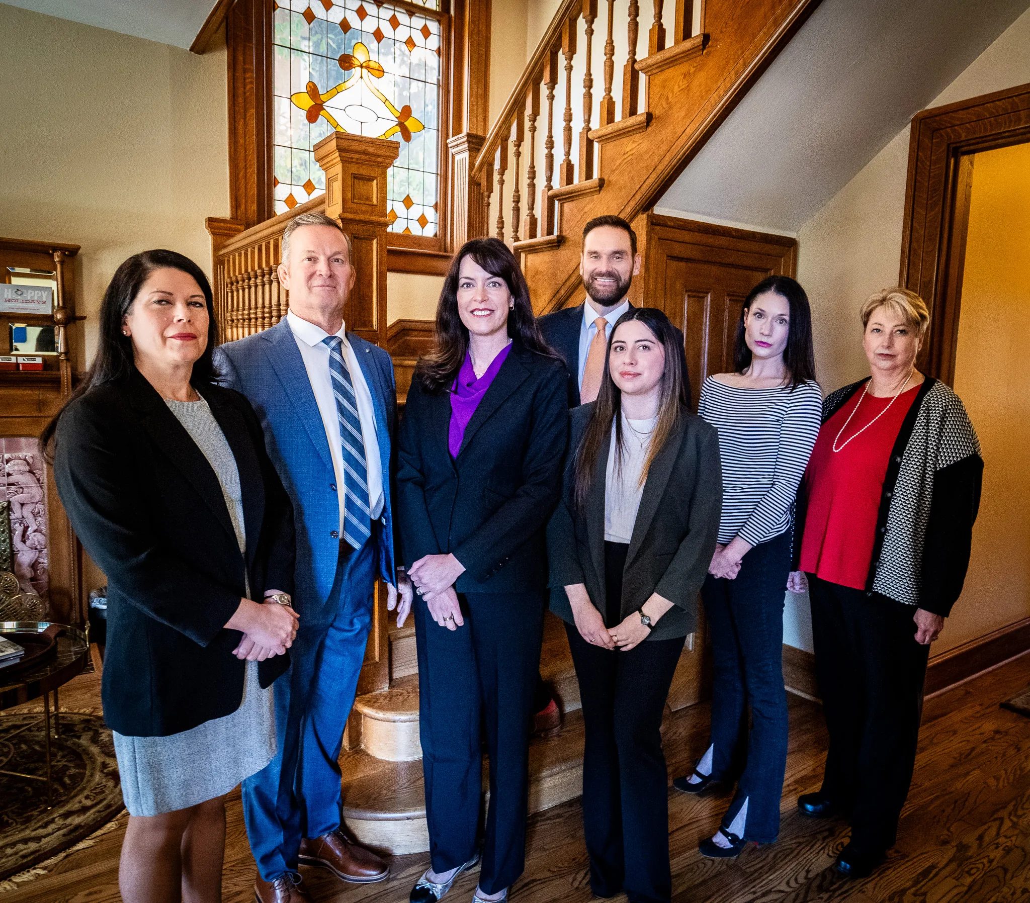 Seven members of the Nelson Law Firm team standing together at the foot of the oak staircase in the firm's Denver office