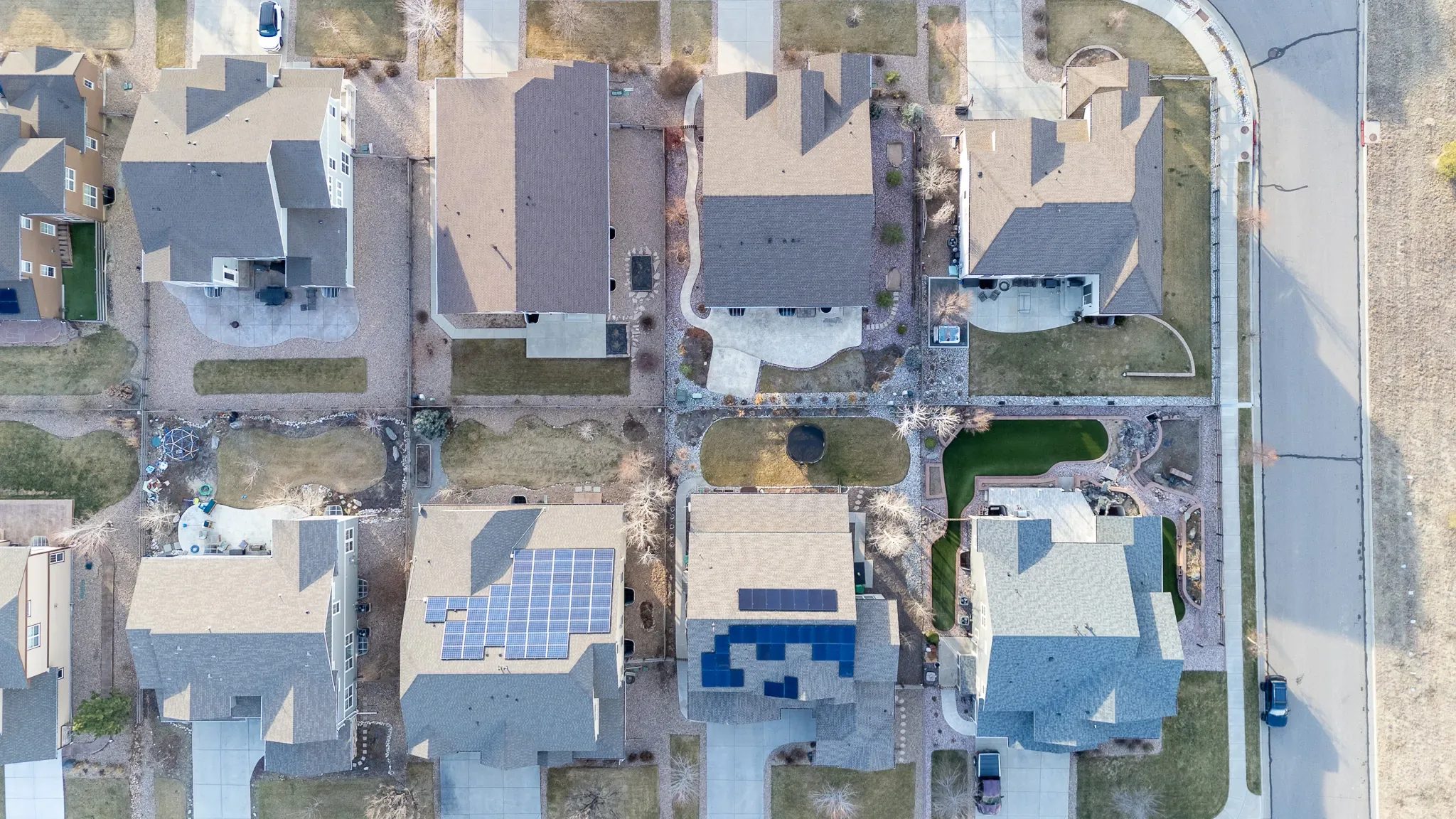 Top-down drone view of a row of suburban homes with rooftop solar panels and landscaped yards in the Denver area.