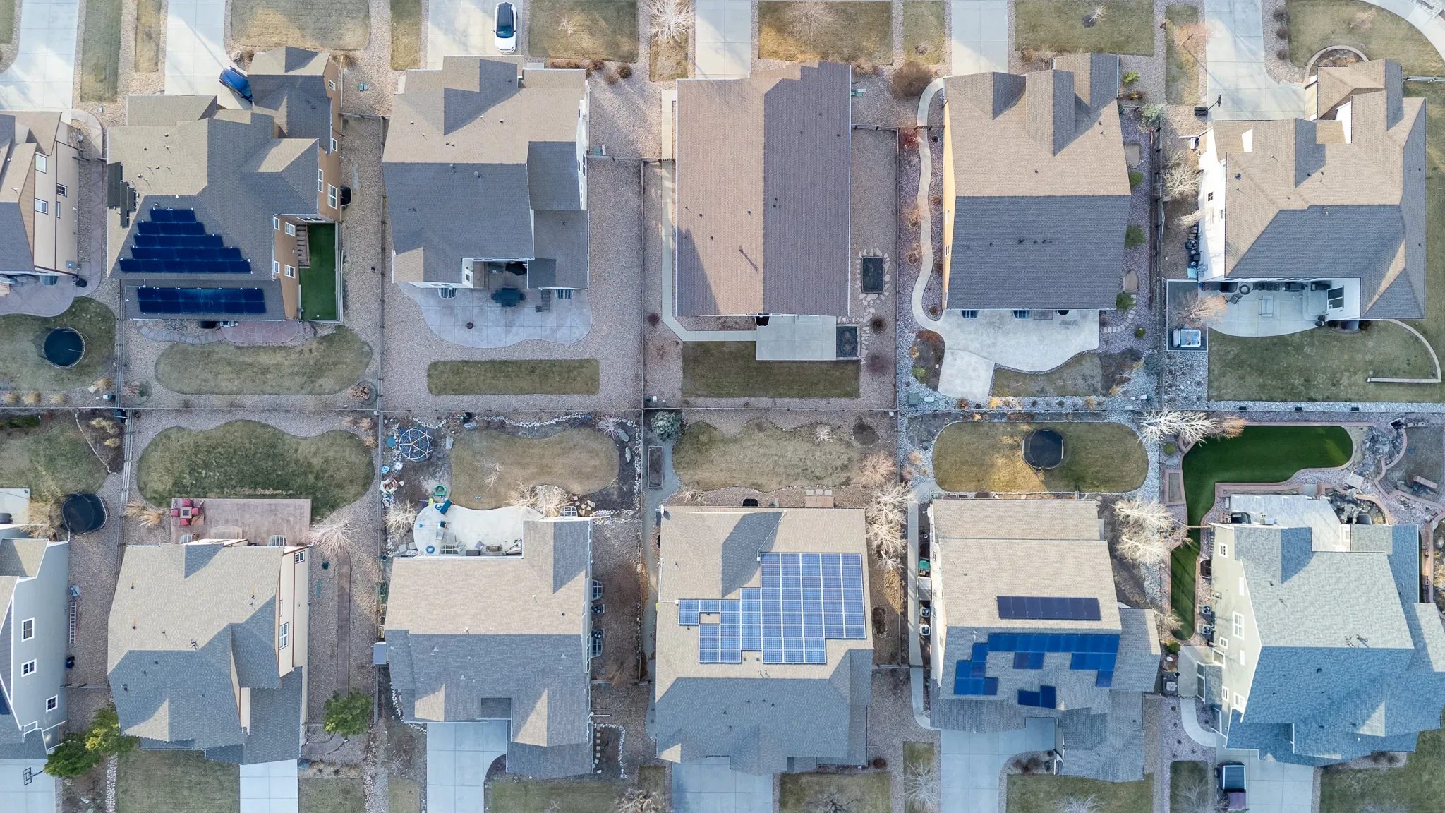 Straight-down aerial of suburban rooftops with solar arrays, patios and small backyards in a Denver-area subdivision.