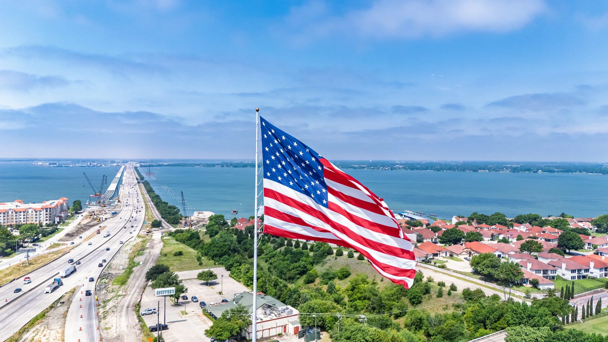 Giant American flag flying beside Interstate 30 in Rockwall, Texas, with Lake Ray Hubbard and the highway bridge beyond
