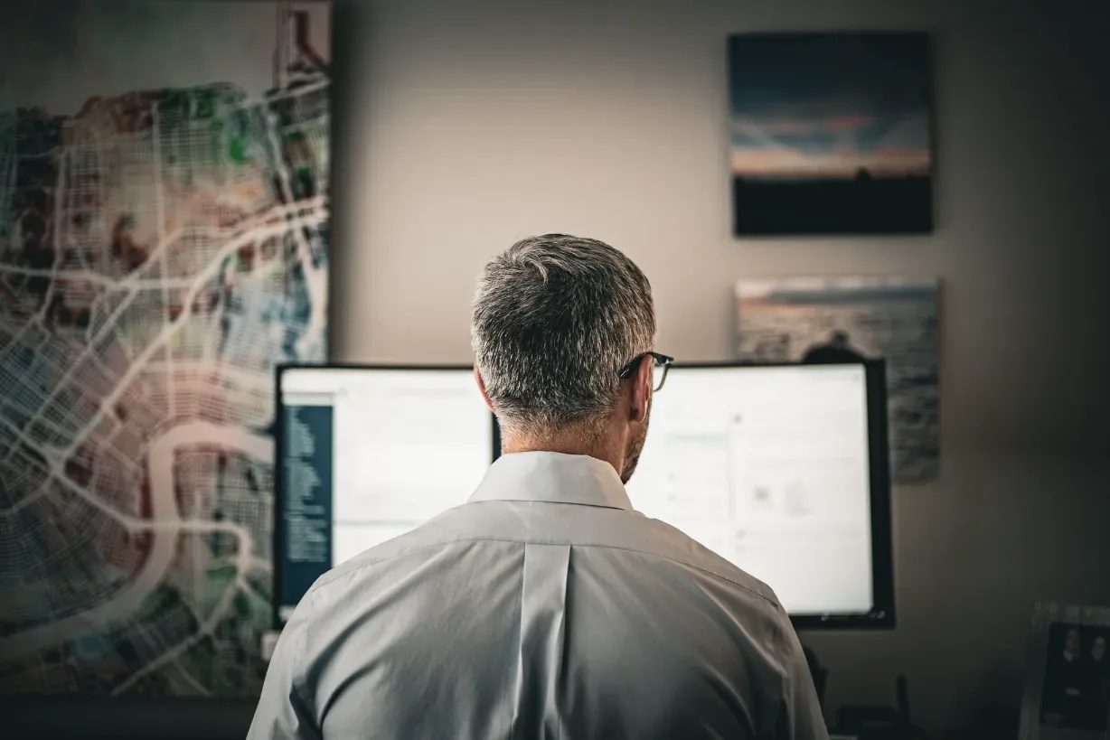 A staff member seen from behind working at a widescreen monitor in a Wick & Trautwein office in Fort Collins, a large city map print on the wall.