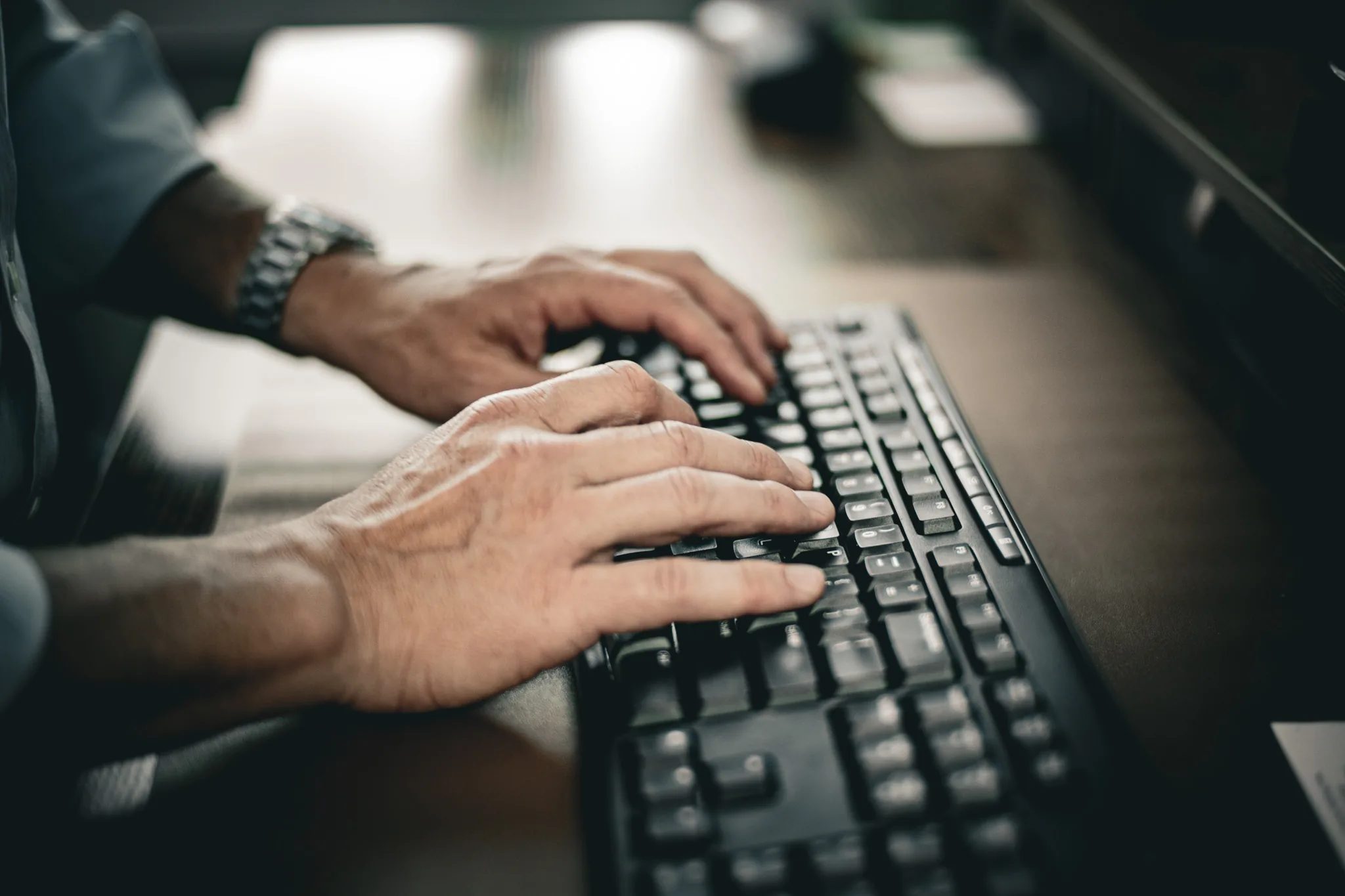 Close-up of hands typing on a black keyboard at a desk in the Wick & Trautwein office in Fort Collins, a wristwatch catching the light.