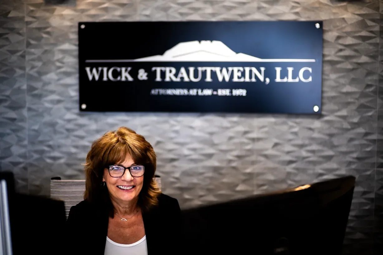 A smiling staff member seated at the front desk beneath the Wick & Trautwein, LLC sign in the firm's Fort Collins office.