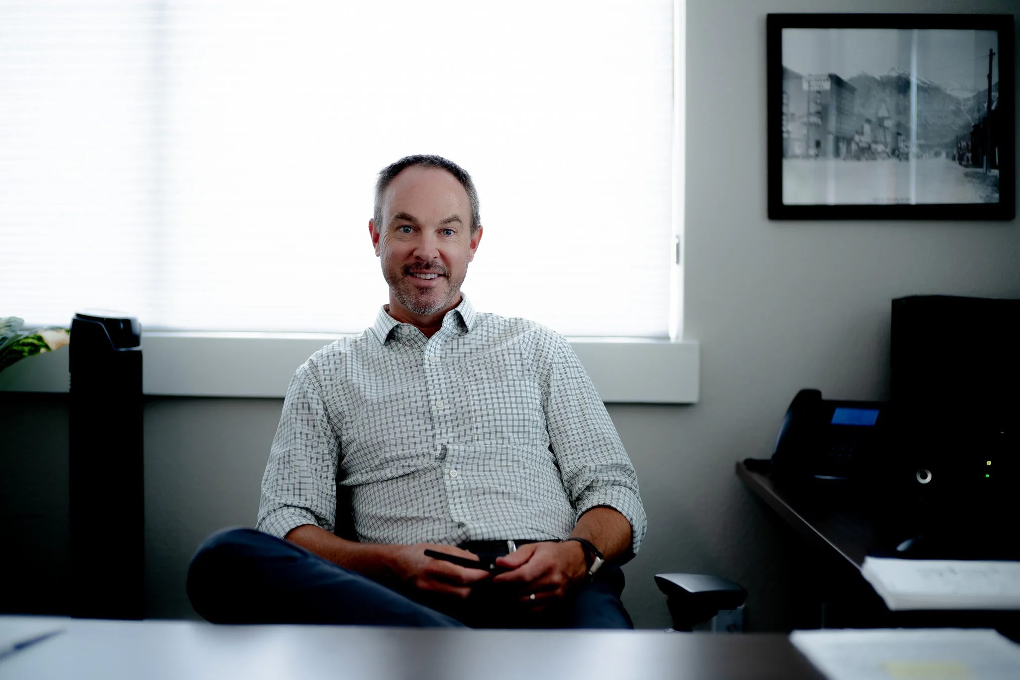 A smiling staff member in a checked shirt seated in an office chair by a bright window in a Wick & Trautwein office in Fort Collins.