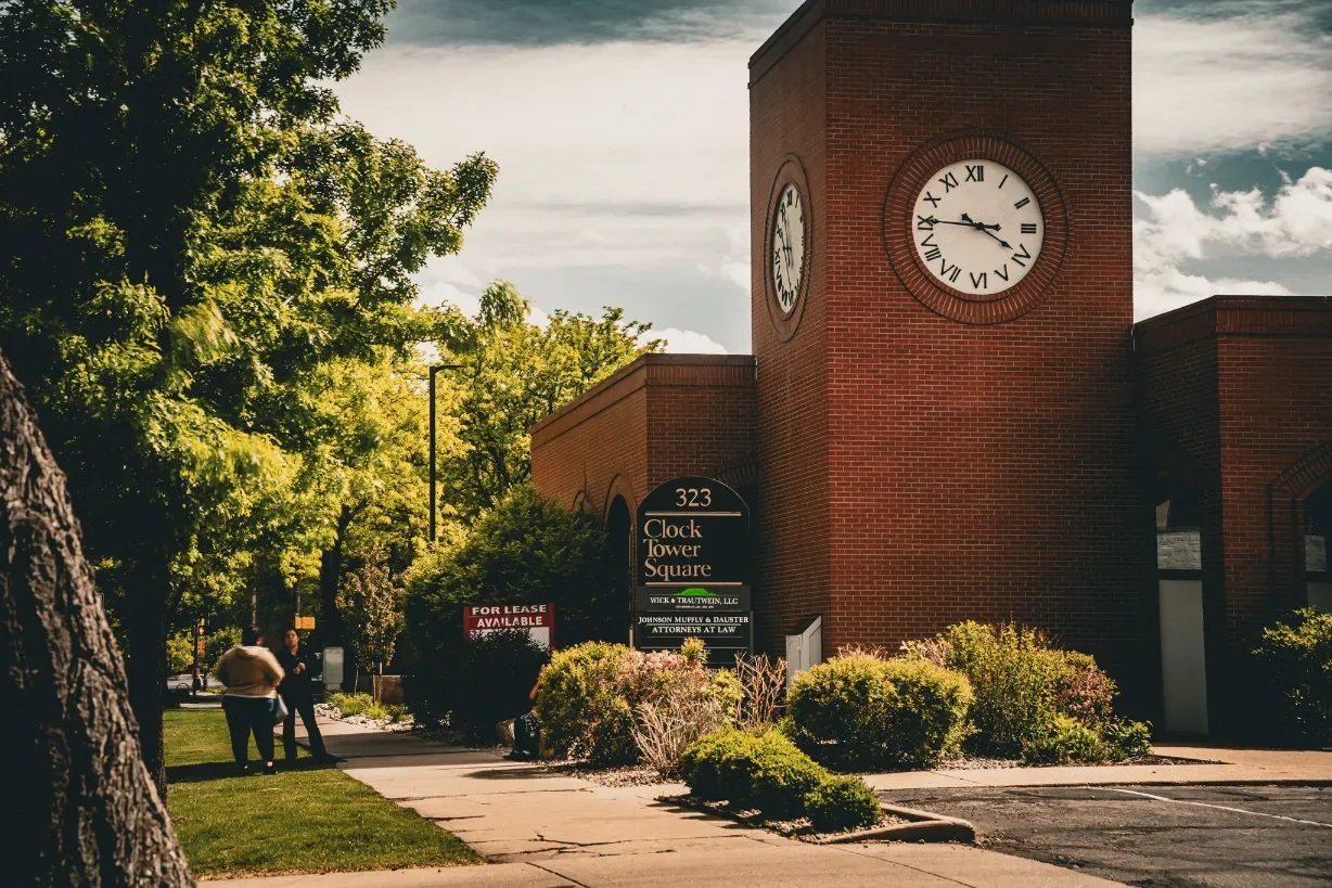 Red brick clock tower at 323 Clock Tower Square in Fort Collins, home to Wick & Trautwein, with a tenant sign and landscaped shrubs.