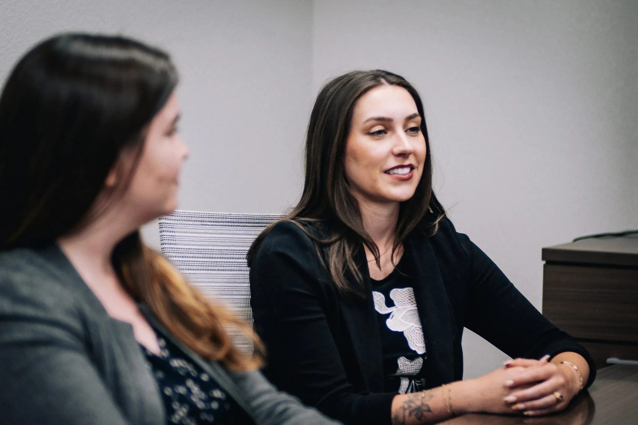 Two staff members seated at the Wick & Trautwein conference table in Fort Collins, one smiling as they listen with hands clasped.