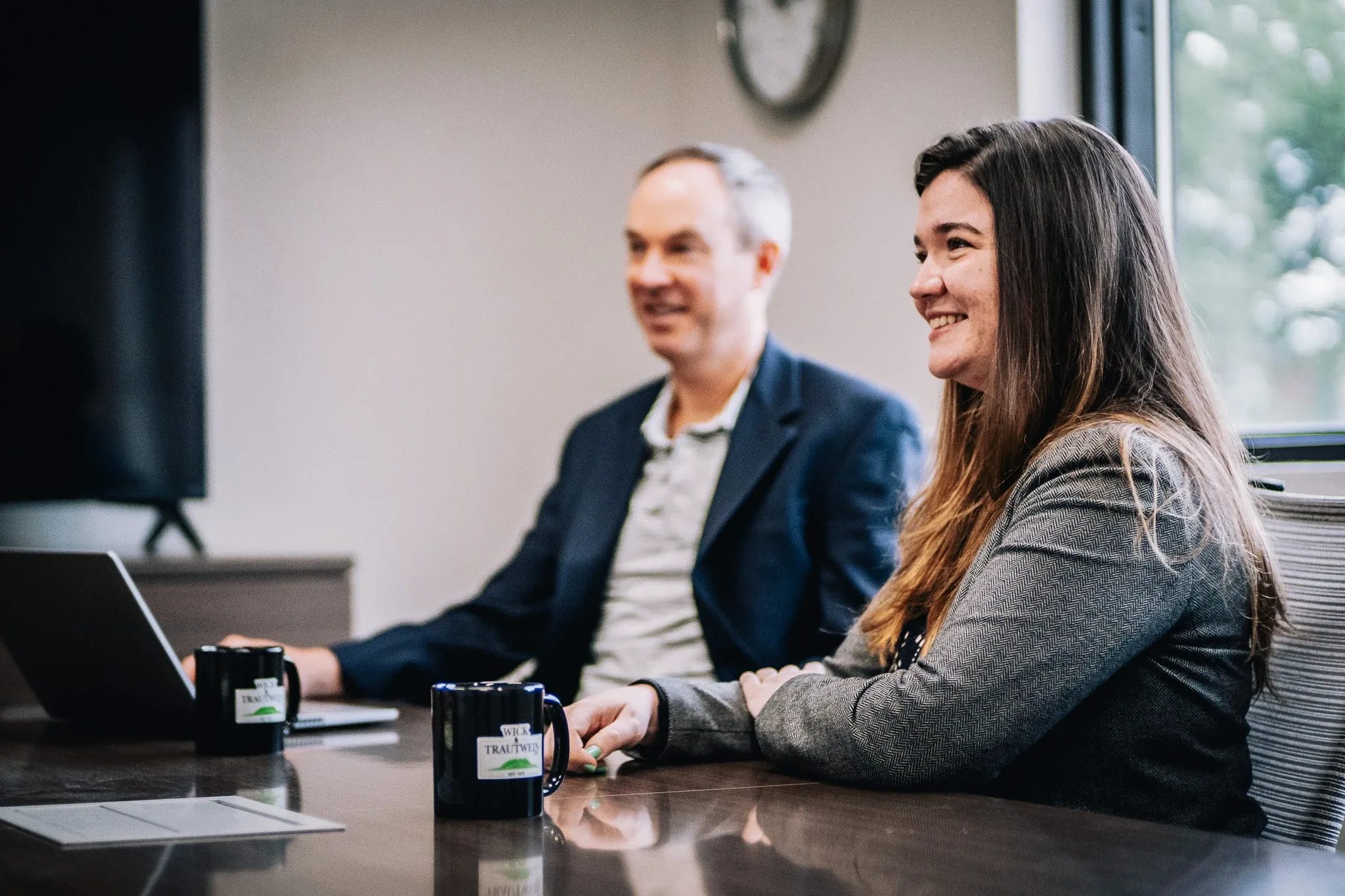 Cassie Williams, attorney at Wick & Trautwein, smiling at a conference table in the firm's Fort Collins office, a colleague at a laptop behind.