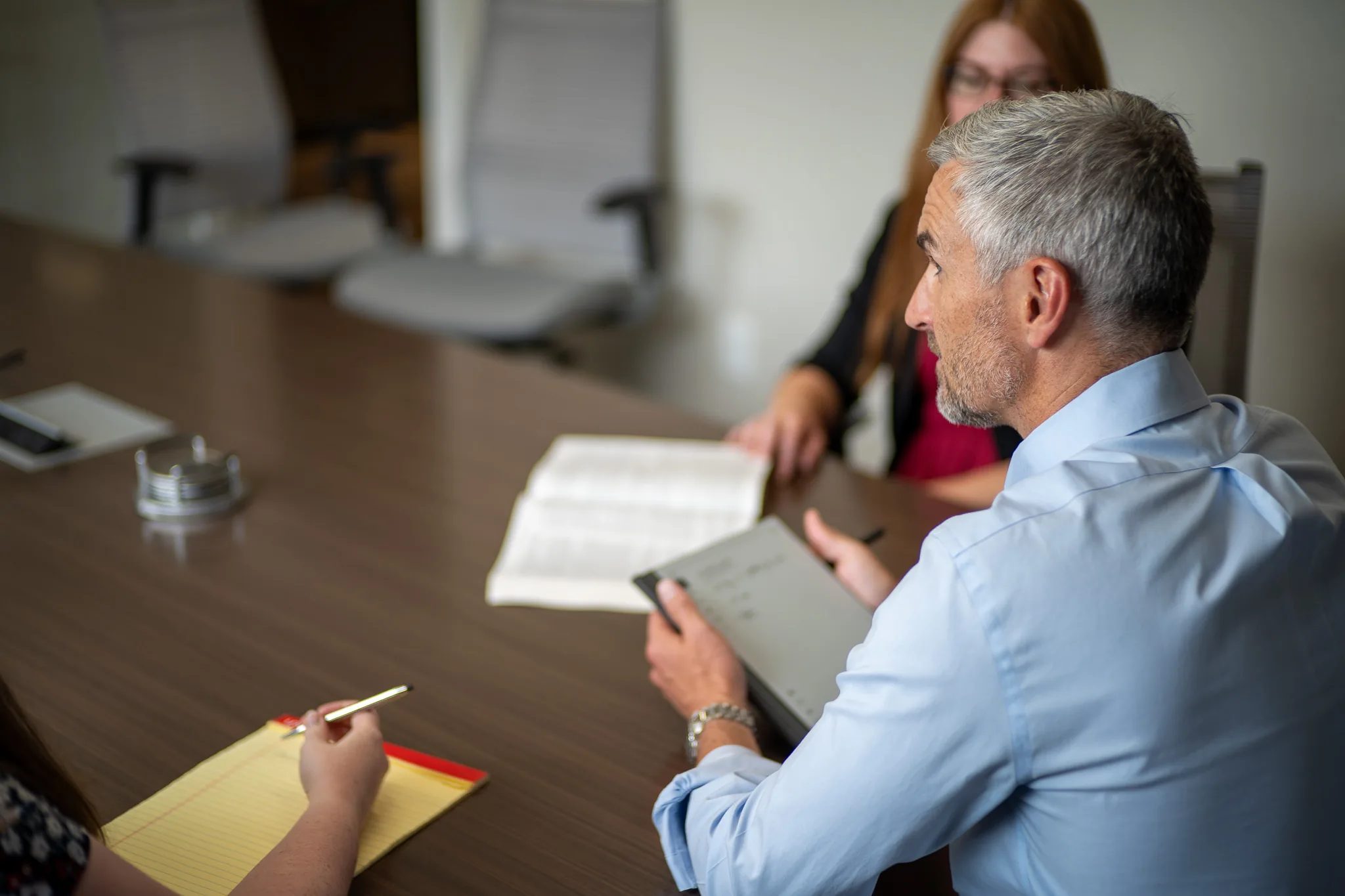 A staff member holding a tablet reviews an open book with two colleagues at the Wick & Trautwein conference table in Fort Collins.