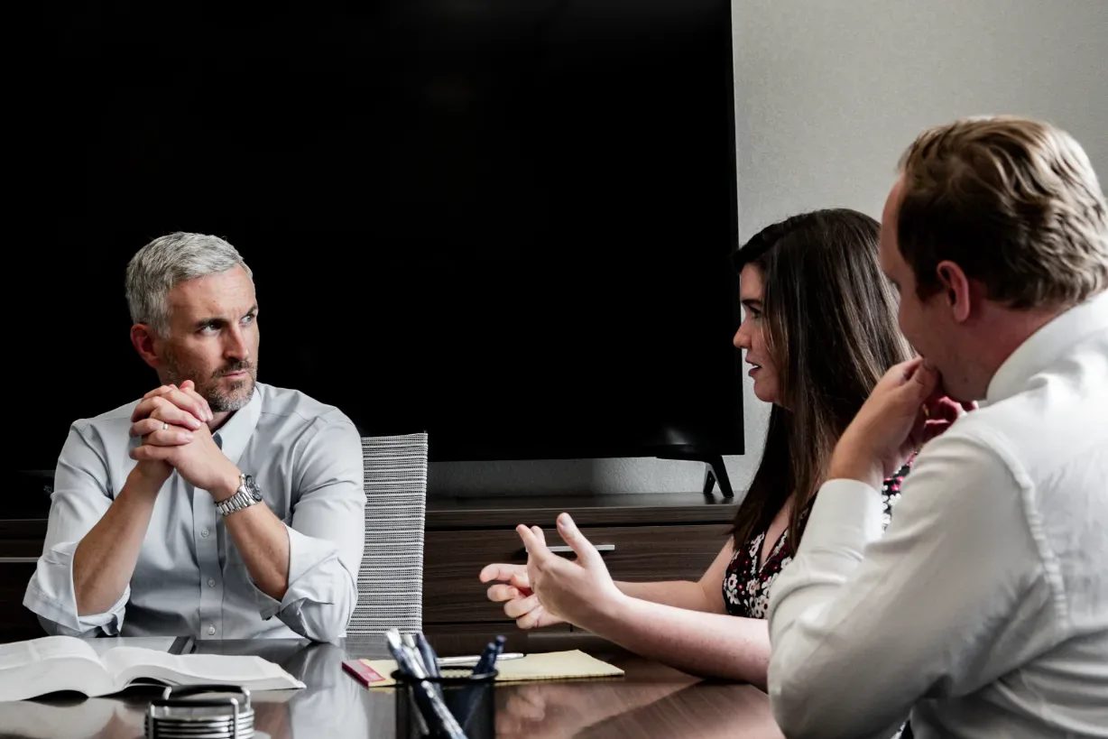Three staff members in discussion at the Wick & Trautwein conference table in Fort Collins, one gesturing while speaking.