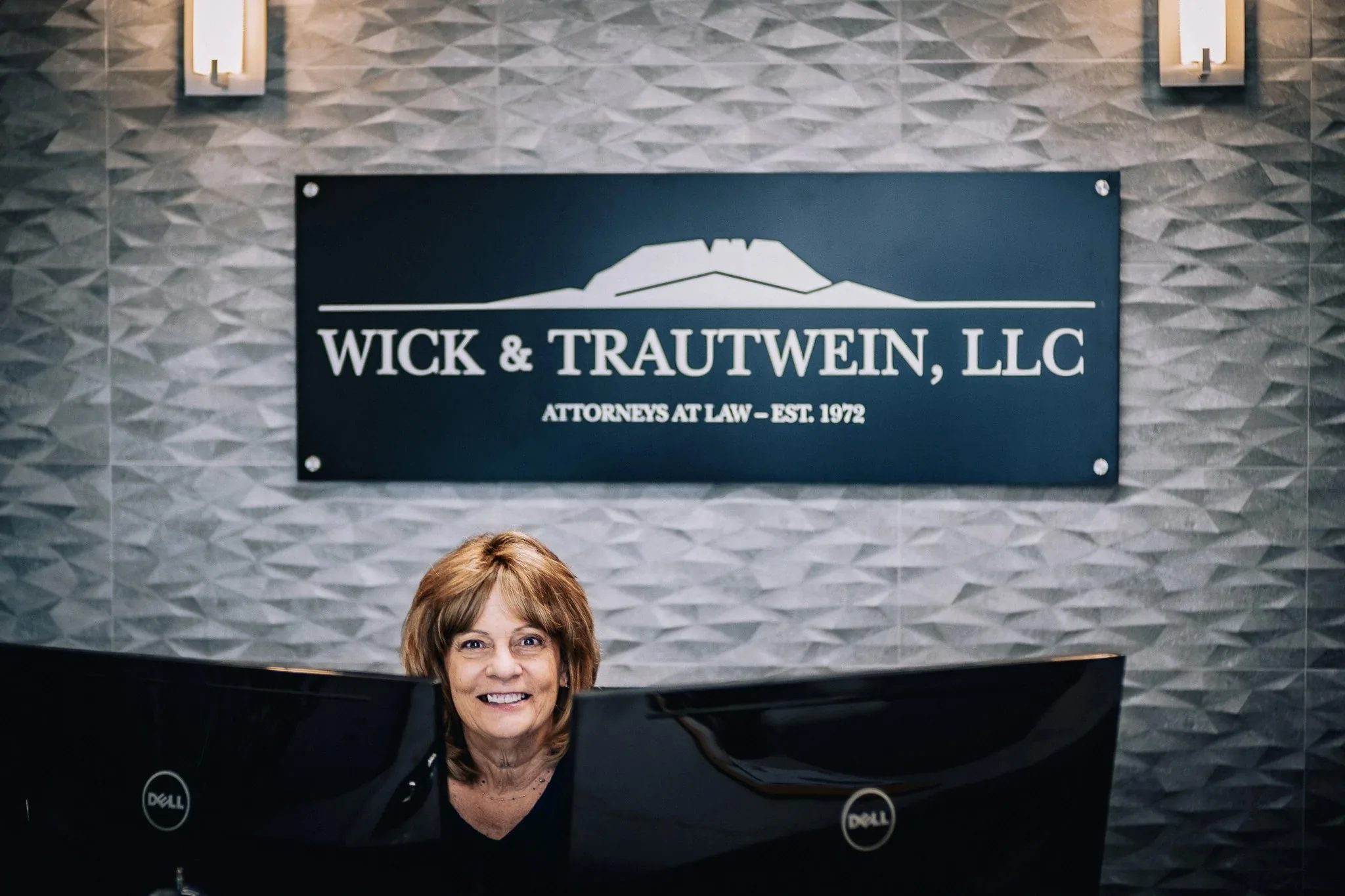 Wick & Trautwein, LLC reception sign on a textured gray tile wall, with a staff member seated at the front desk below in Fort Collins.