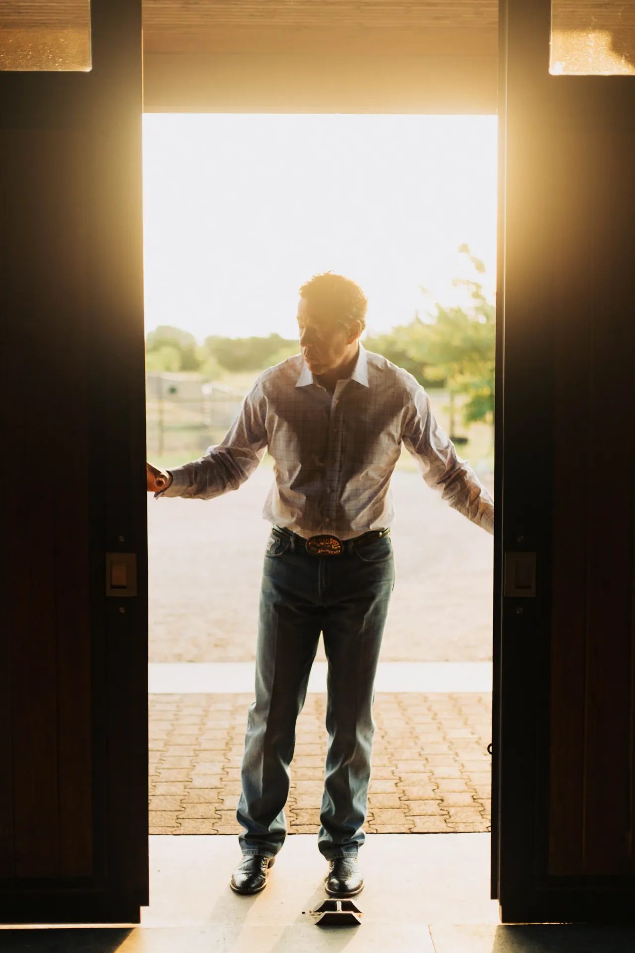 A person stands silhouetted in an open barn doorway with sunlight flaring behind them.