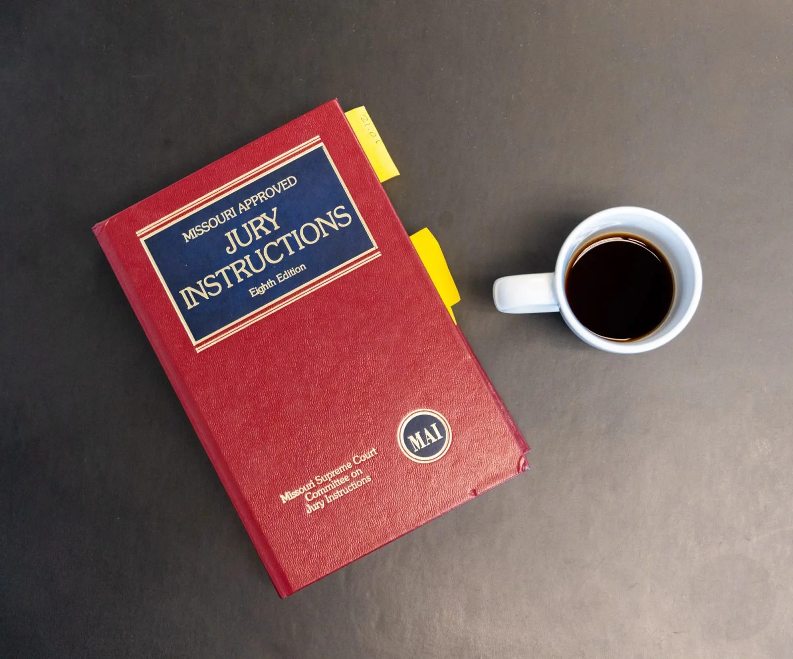 A red jury instructions law book sits beside a cup of black coffee on a desk, seen from above.