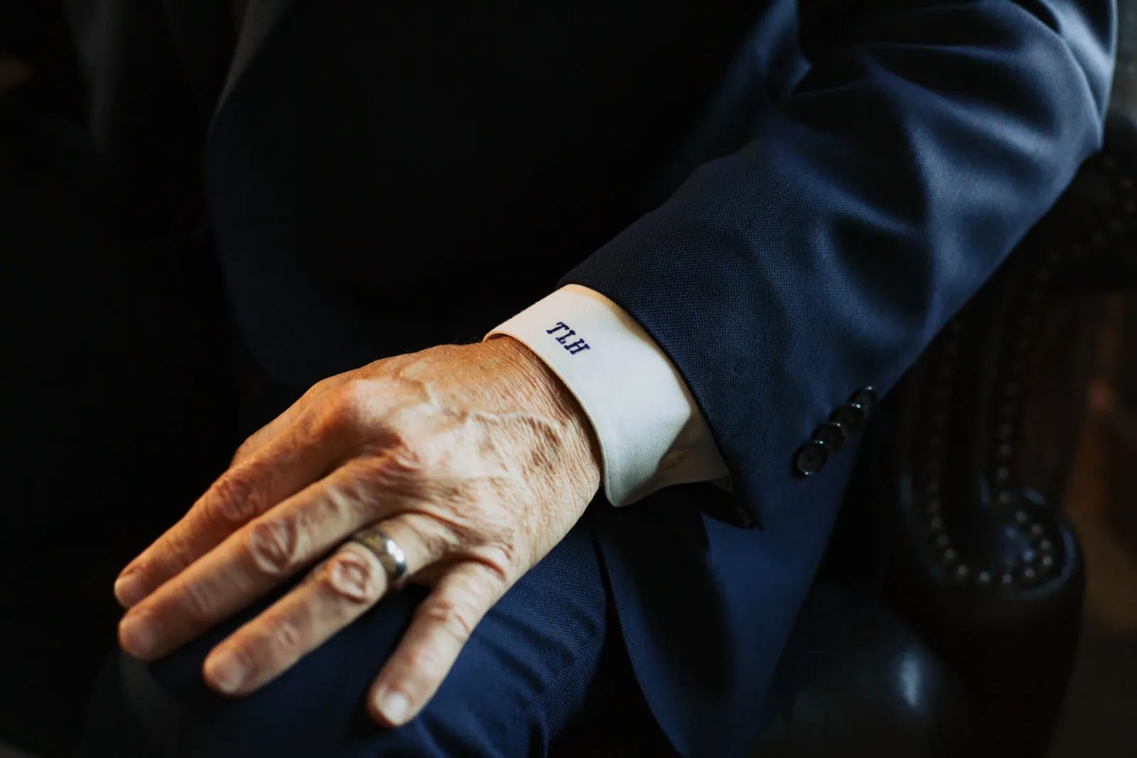 A close view of a monogrammed shirt cuff and ring on a navy suit sleeve.