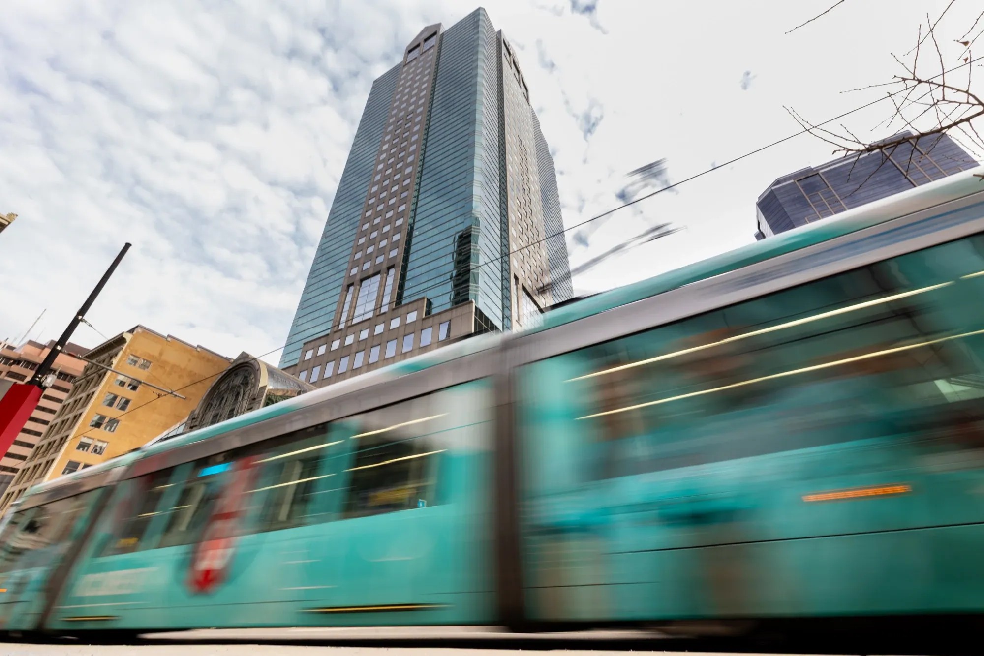 A light rail train streaks past a downtown high-rise at dusk in a long exposure.