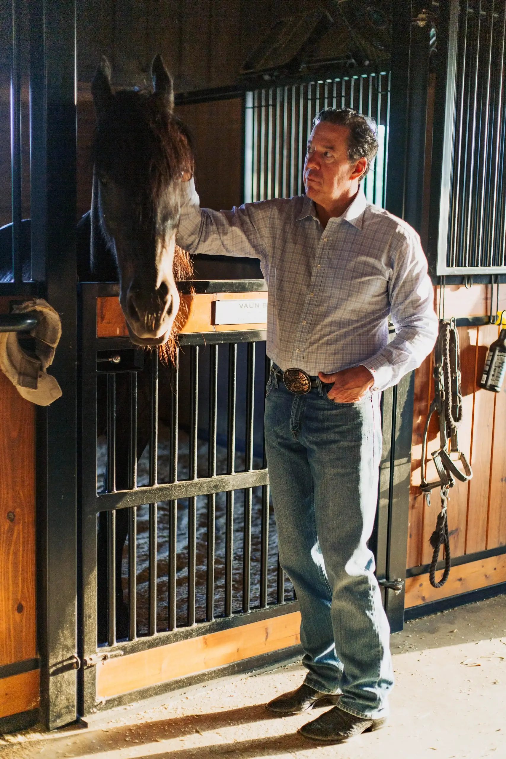 Tim Hartley rests a hand on a dark horse leaning out over its stall door.