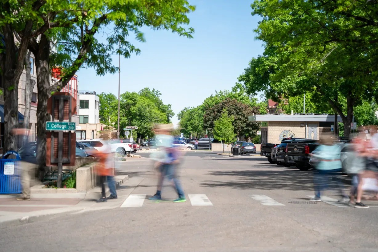 People blurred in motion cross a street beside a South College Avenue sign, under summer trees.